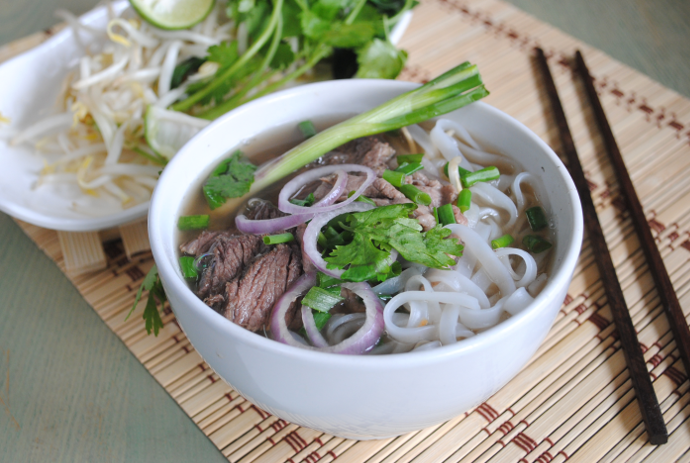 bowl of noodle with clear aromatic broth rice noodles sliced beef fresh herbs